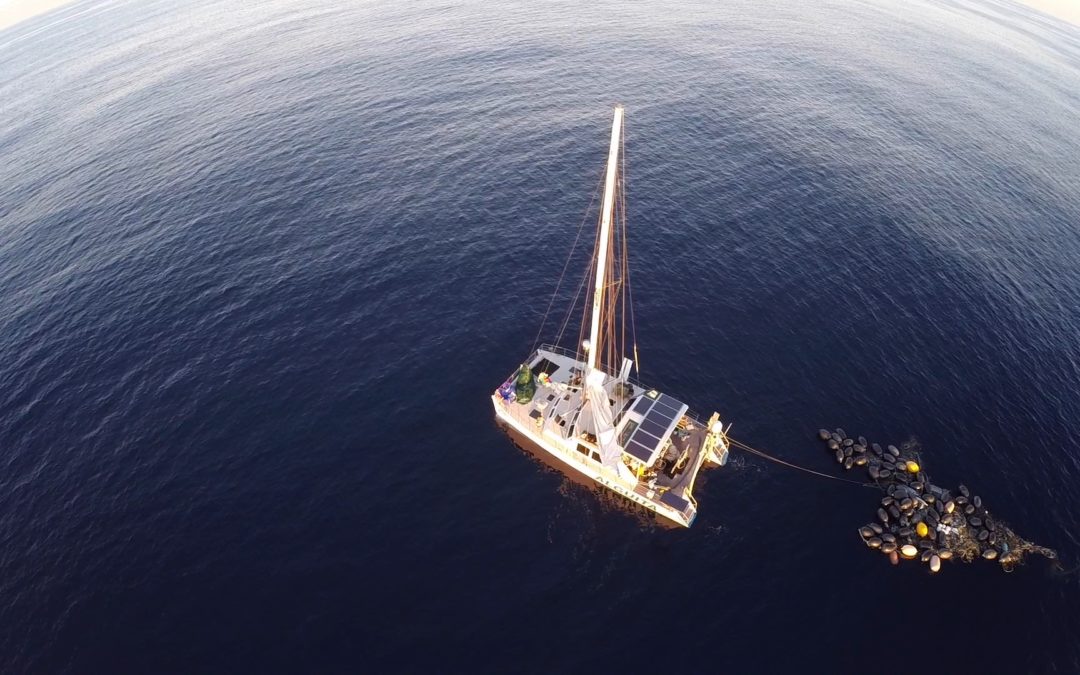 Drone shot of a Catamaran sailboat towed to a massive plastic debris clump