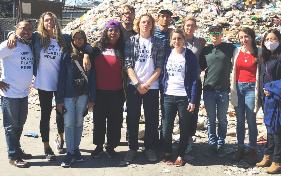 A group of 12 people standing together in front of a pile of plastic trash