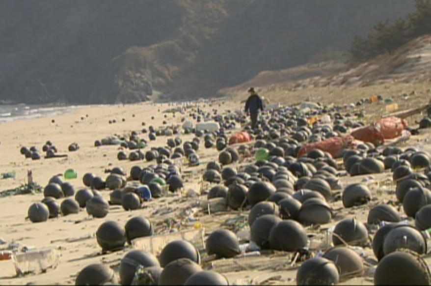 A person walks along a beach littered with large black buoys and other plastic litter