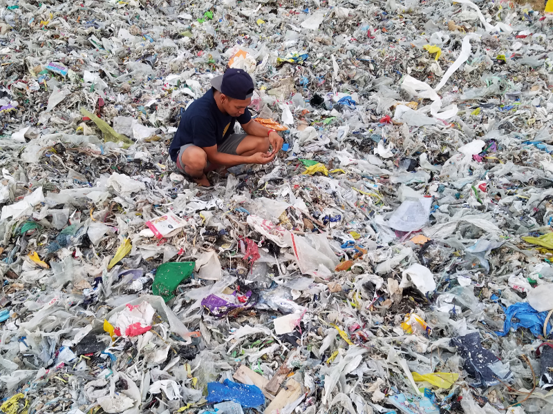 Worker sits among plastic waste sorting pieces.