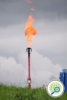 A red pipe sticking up from the ground emitting a large flame.