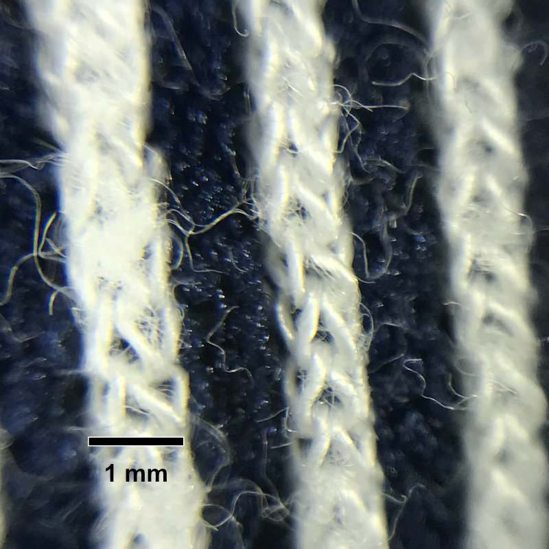 Magnified image of a knitted shirt with blue and white stripes showing individual microfibers. 1 mm scale bar.
