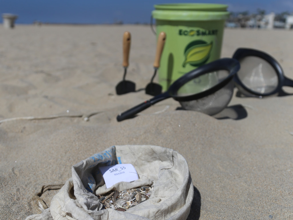 A bucket, two spades, two sifters and a cloth bag sit on the sand.