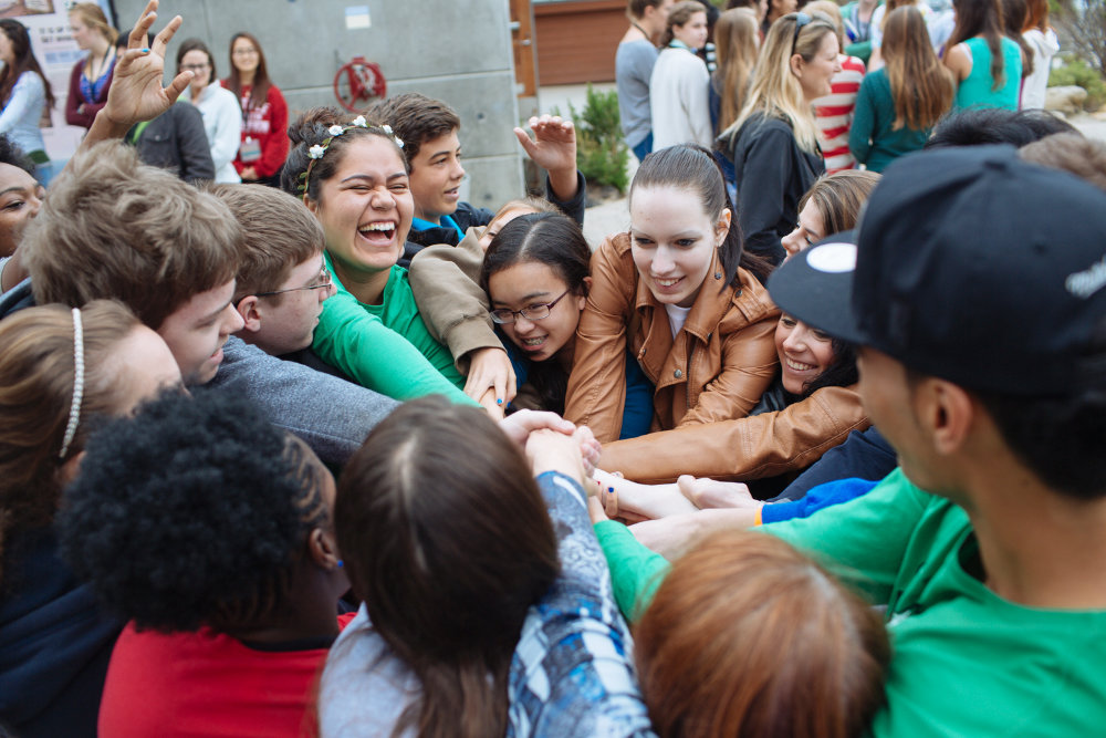 7N0A8895-web A group of students huddle in a circle with their hands reached out into the middle