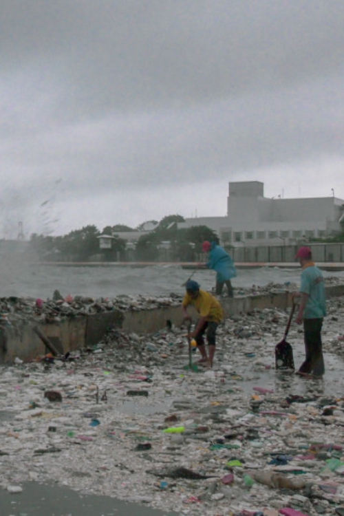 Workers sweep plastic debris washing over seawall