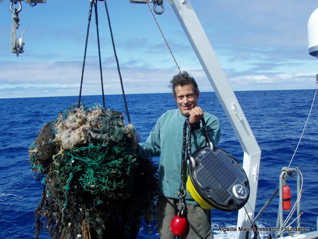 Captain Moore holds stands next to a ghost net hauled from the ocean