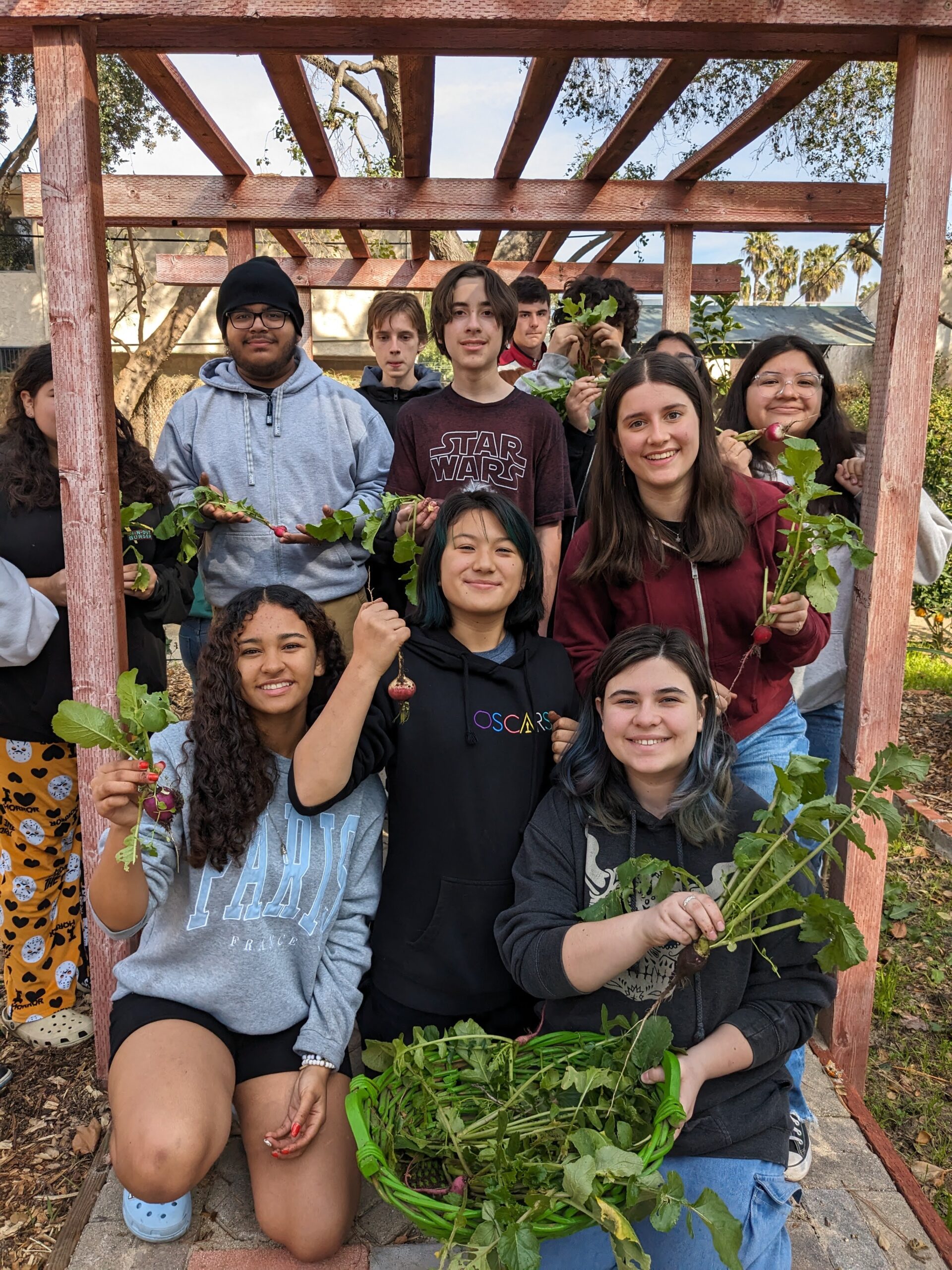 Students in the school garden proudly holding their harvest of organic vegetables